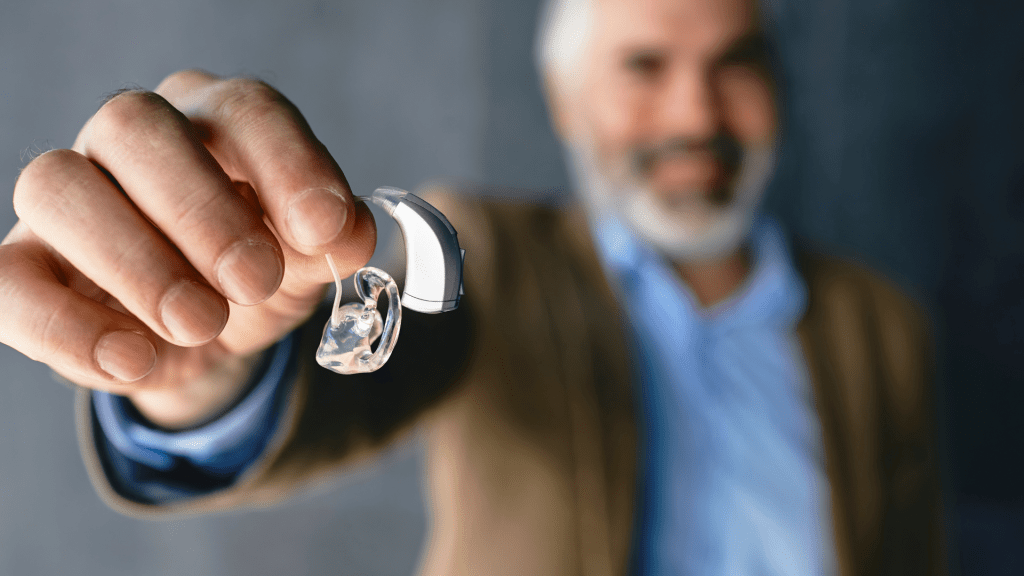 Aide auditive BTE tenu en main, avec embout transparent et courbure derrière l’oreille.