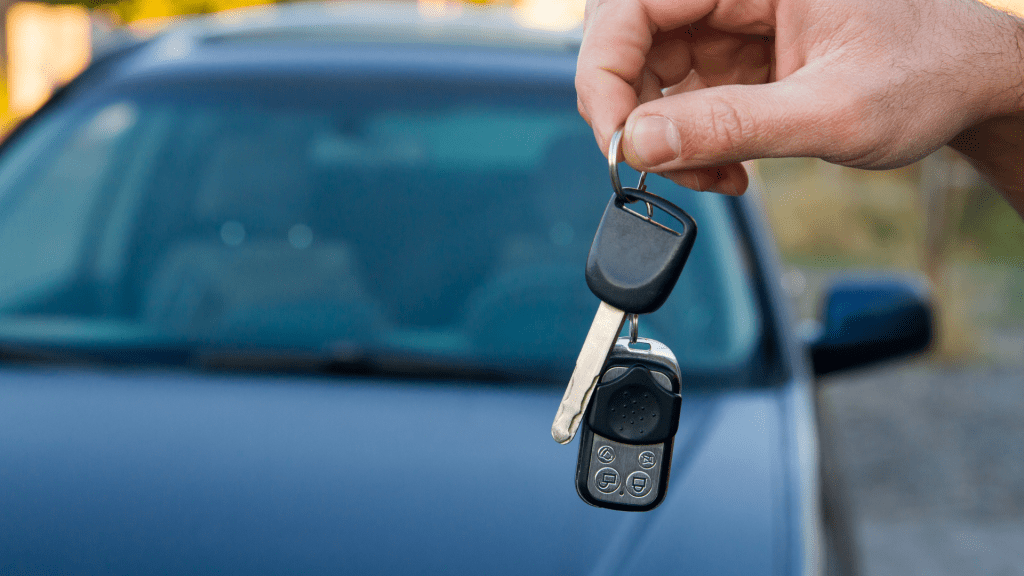 Une main tenant des clés de voiture devant un véhicule bleu, symbolisant la remise ou la possession d’un véhicule dans le cadre d’un contrat de financement LOA.
