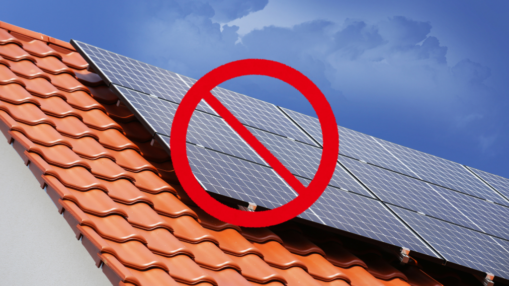 Toiture en tuiles avec des panneaux photovoltaïques barrés d’un symbole d’interdiction, illustrant un litige lié à une installation solaire et à des pratiques commerciales déloyales.