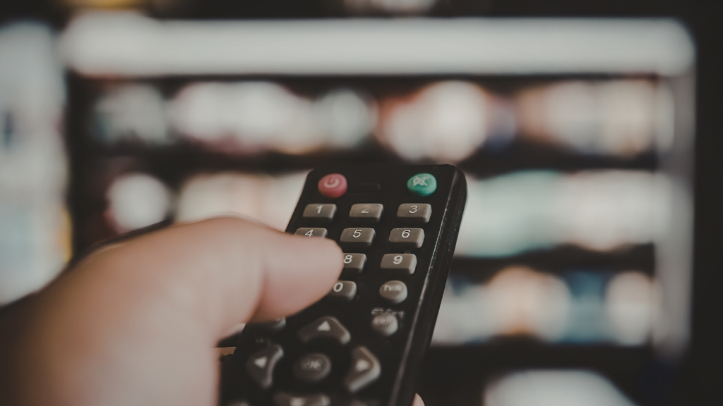 Main tenant une télécommande pointée vers un téléviseur flou, illustrant un litige lié à un abonnement Canal+ souscrit sans consentement.
